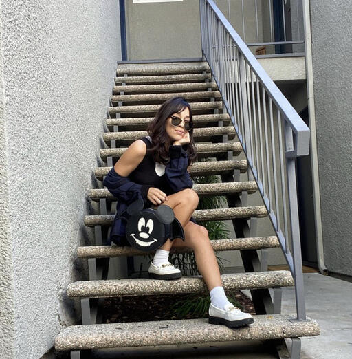Woman sitting on stairs outside holding a Mickey Mouse bat crossbody bag.